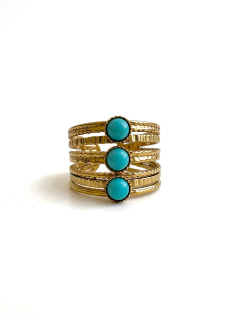 Three stacked gold rings with textured bands and three vertical rows of round turquoise cabochon stones, set against a plain white background.