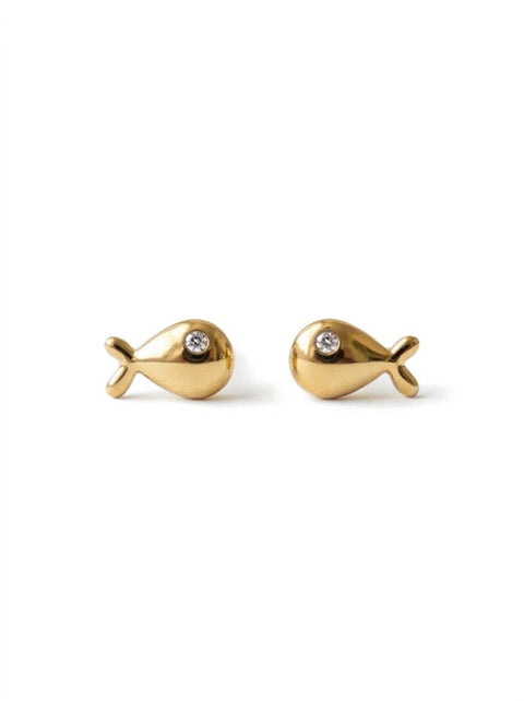 A pair of gold fish-shaped stud earrings, each featuring a small clear round gemstone set in the center, displayed on a clean white background.
